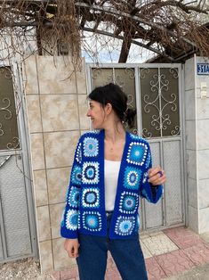 a woman standing in front of a building wearing a blue crocheted cardigan