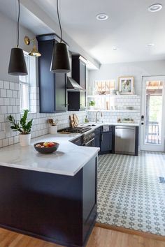 a kitchen with black cabinets and white counter tops, an island in the middle has a bowl of fruit on it