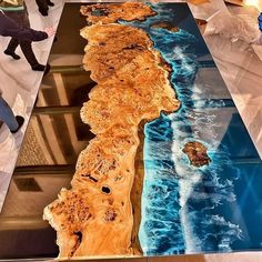 the table is made out of wood and has an ocean scene on it, as well as two people walking by