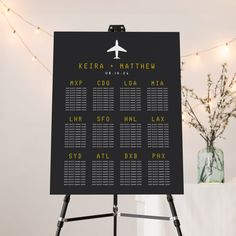 a black and white wedding seating chart on a tripod stand with lights in the background