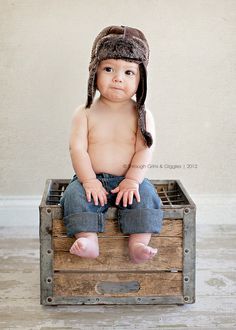 a baby sitting on top of a wooden crate wearing a hat and looking at the camera