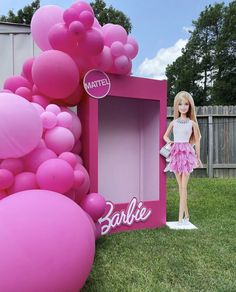 a barbie doll is standing in front of a barbie box with balloons on the lawn