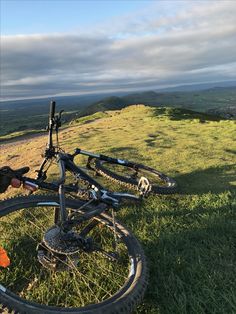 a bicycle that is laying on the ground in the grass with mountains in the background