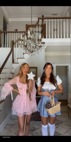 two women dressed in costume standing next to each other near stairs and chandelier