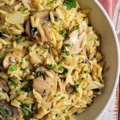 pasta with mushrooms and parsley in a white bowl on a pink towel next to a fork