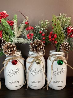 three mason jars decorated with pine cones and evergreens