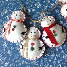 three snowman ornaments hanging from a string on a blue background with snowflakes