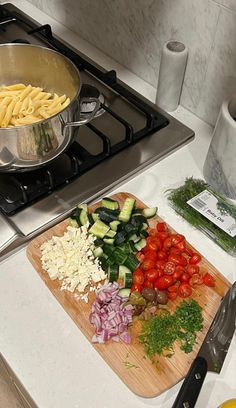 a wooden cutting board topped with lots of veggies next to a stove top