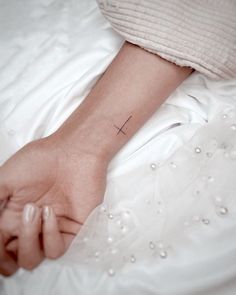 a woman's arm with a small cross tattoo on her left wrist, resting on a bed