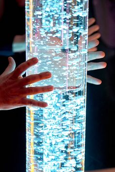 two hands reaching out from behind a tall glass tube with glowing lights on the bottom