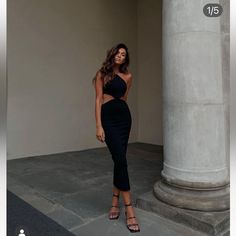 a woman standing in front of a pillar wearing a black dress with cutouts on the sides