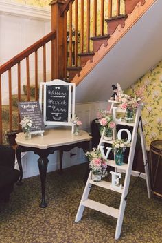 a small table with flowers on it next to a stair case and sign that says welcome