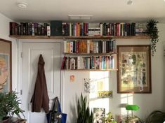 a bookshelf filled with lots of books next to a white door and potted plants