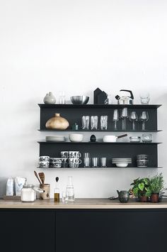 a kitchen with black cabinets and shelves filled with dishes, cups and utensils