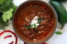 a bowl filled with meat and vegetables on top of a white cloth next to green peppers