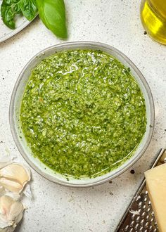 a bowl filled with green pesto next to garlic and cheese