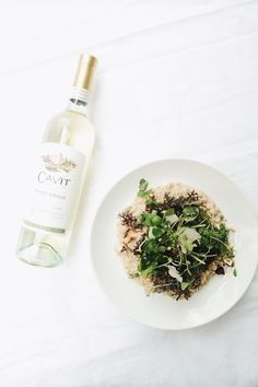 a white plate topped with rice and veggies next to a bottle of wine