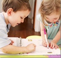 two young children are sitting at a table and doing something on paper with a marker