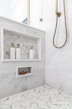 a bathroom with white marble tile and gold faucet shower head in the corner