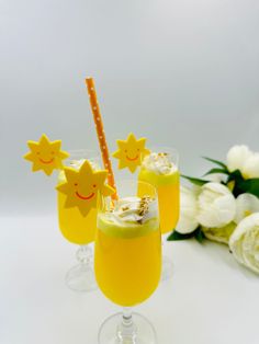 two glasses filled with yellow liquid and topped with straws next to white flowers on a table