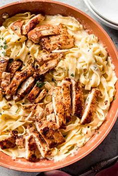 an orange bowl filled with chicken alfredo and sauce on top of a marble countertop