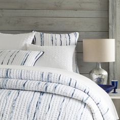 a bed with white and blue comforters in a bedroom next to a lamp on a table