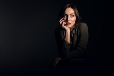 a woman is sitting in the dark with her hand on her chin and looking at the camera