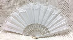 a white fan sitting on top of a table next to a lace covered wallpaper