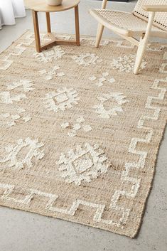 an area rug with white and beige designs on the floor next to a wooden chair