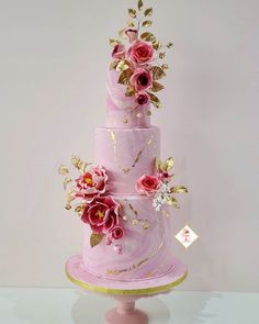 a three tiered cake with pink frosting and gold flowers on the top layer