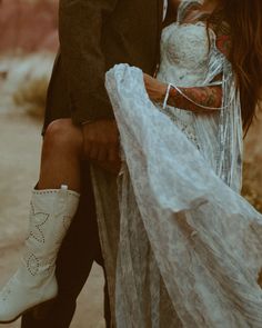 a man and woman standing next to each other in the desert wearing white cowboy boots