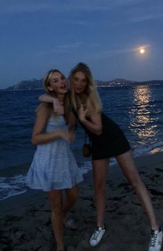 two young women standing on the beach at night, one holding her arm around the other's neck