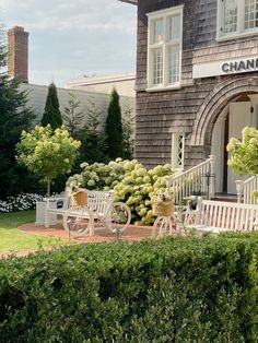 a house that has some chairs in front of it and bushes around the outside area