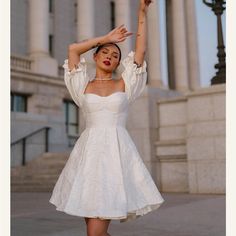 a woman in a short white dress is posing for the camera with her hands up