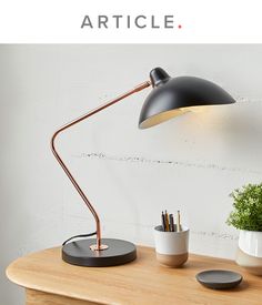 a desk lamp sitting on top of a wooden table next to a potted plant