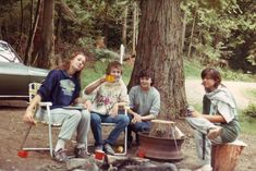 four people sitting around a fire pit in the woods