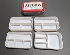 four white trays with compartments on top of a black table next to an altoids tin