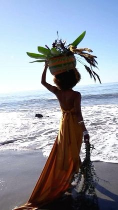 a woman standing on top of a beach next to the ocean wearing a dress and headpiece