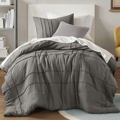 a bed with grey and white comforters in a bedroom next to a yellow chair