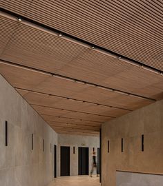 an empty room with wooden ceiling and concrete walls on either side is a person walking in the distance