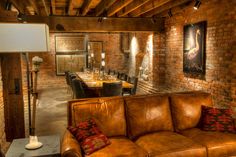 a couch and table in a room with brick walls, chairs and pictures on the wall