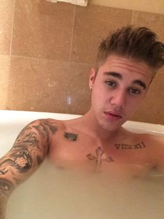 a man with tattoos sitting in a bathtub