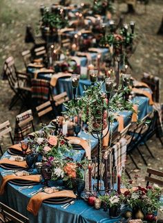 a long table is set up with blue linens and greenery for an outdoor dinner