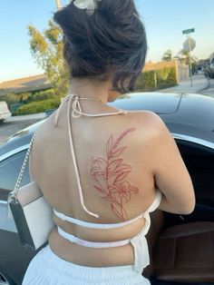 a woman with a flower tattoo on her back is getting out of a car and looking at the street