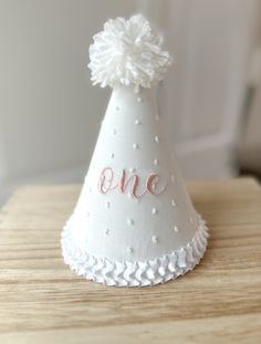 a small white party hat with the word one on it's side and a pom - pom at the top