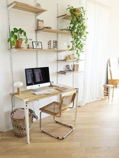 a desk with a computer on top of it in front of a window and bookshelves