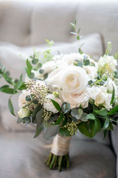 a bridal bouquet on a couch with greenery and white flowers in the foreground