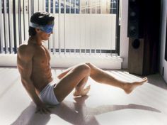 a shirtless man sitting on the floor in front of a window wearing a blindfold