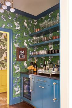 a kitchen with blue cabinets and green wallpaper on the walls is decorated with birds