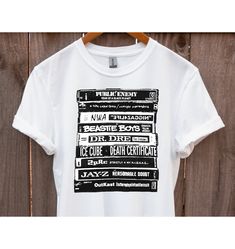 a white t - shirt hanging on a wooden wall with black and white text in it